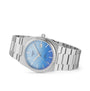 The Tissot PRX Powermatic 80 is a silver metal wristwatch with a blue textured dial and date display, shown against a white background.