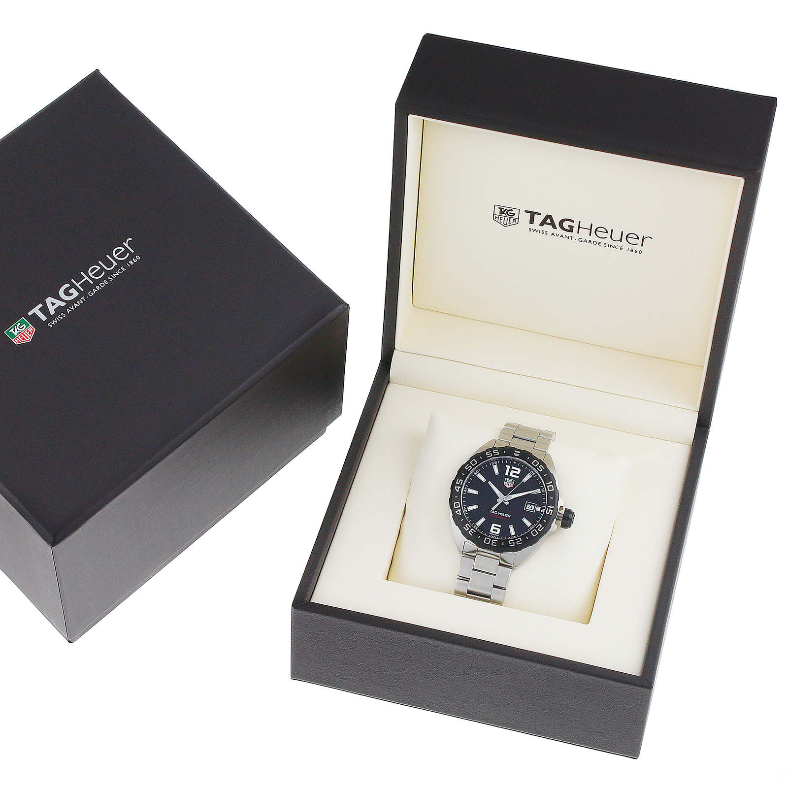 A TAG Heuer Formula 1 Date watch is shown with a black dial and stainless steel case, displayed in an open branded box beside its closed outer packaging.