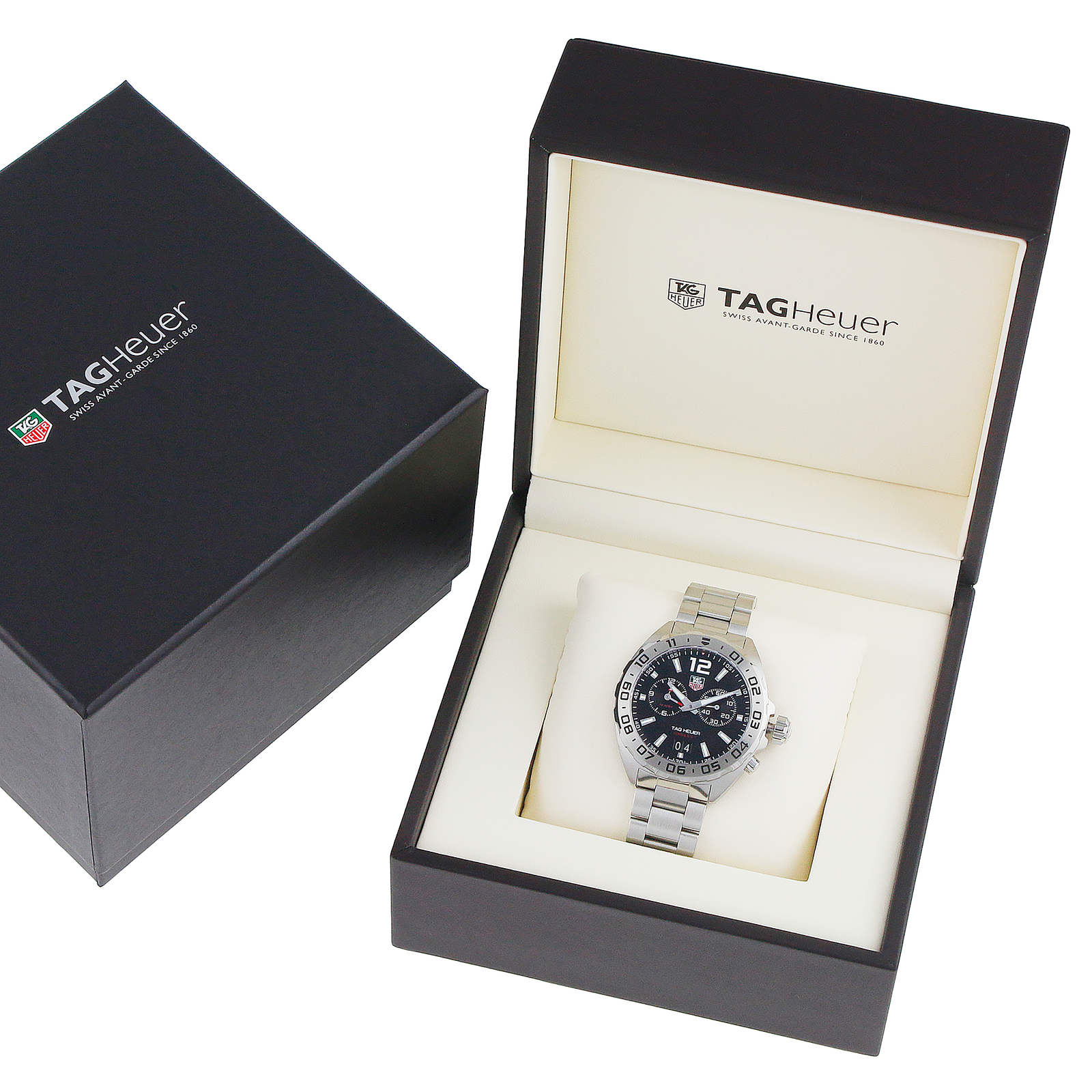 A TAG Heuer Formula 1 Date watch with a metal band is shown in an open branded box, with a closed TAG Heuer box placed next to it.