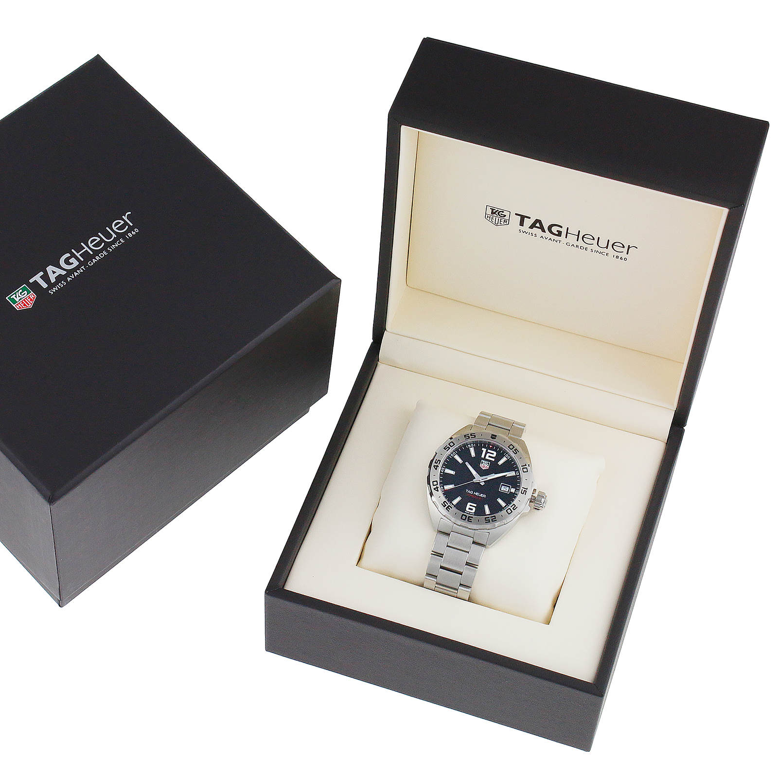 A TAG Heuer Formula 1 Date wristwatch with a silver metal band and black dial is displayed in an open black box, highlighting its precise quartz movement, with a closed box placed nearby.