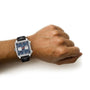 A person wearing a TAG Heuer Monaco Chronograph with a square case, blue dial, and black leather strap on their left wrist, evoking Steve McQueen’s iconic style, set against a white background.
