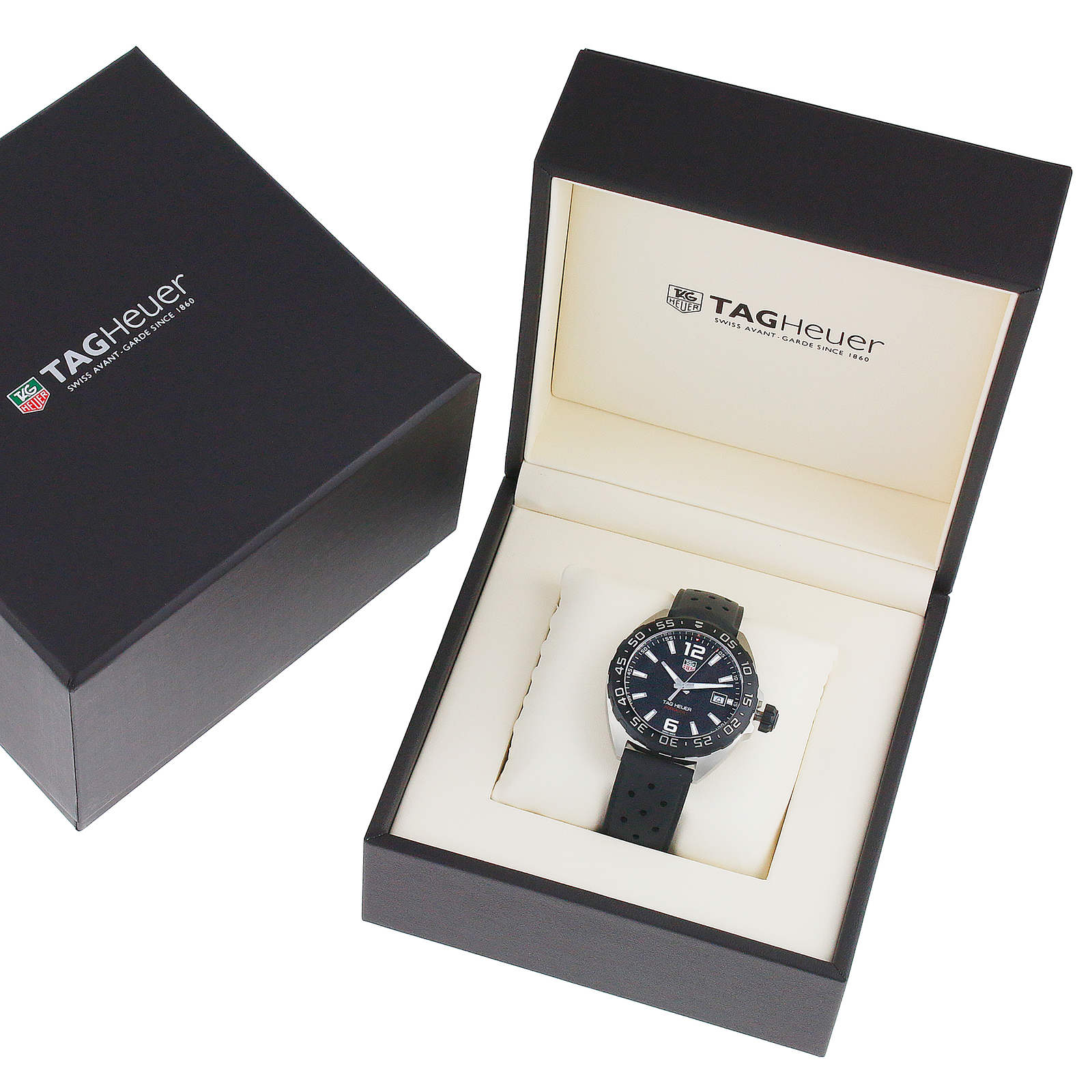 A TAG Heuer Formula 1 Date watch with a black strap is showcased in an open branded box, emphasizing its refined quartz movement, with the box lid and outer packaging placed nearby.