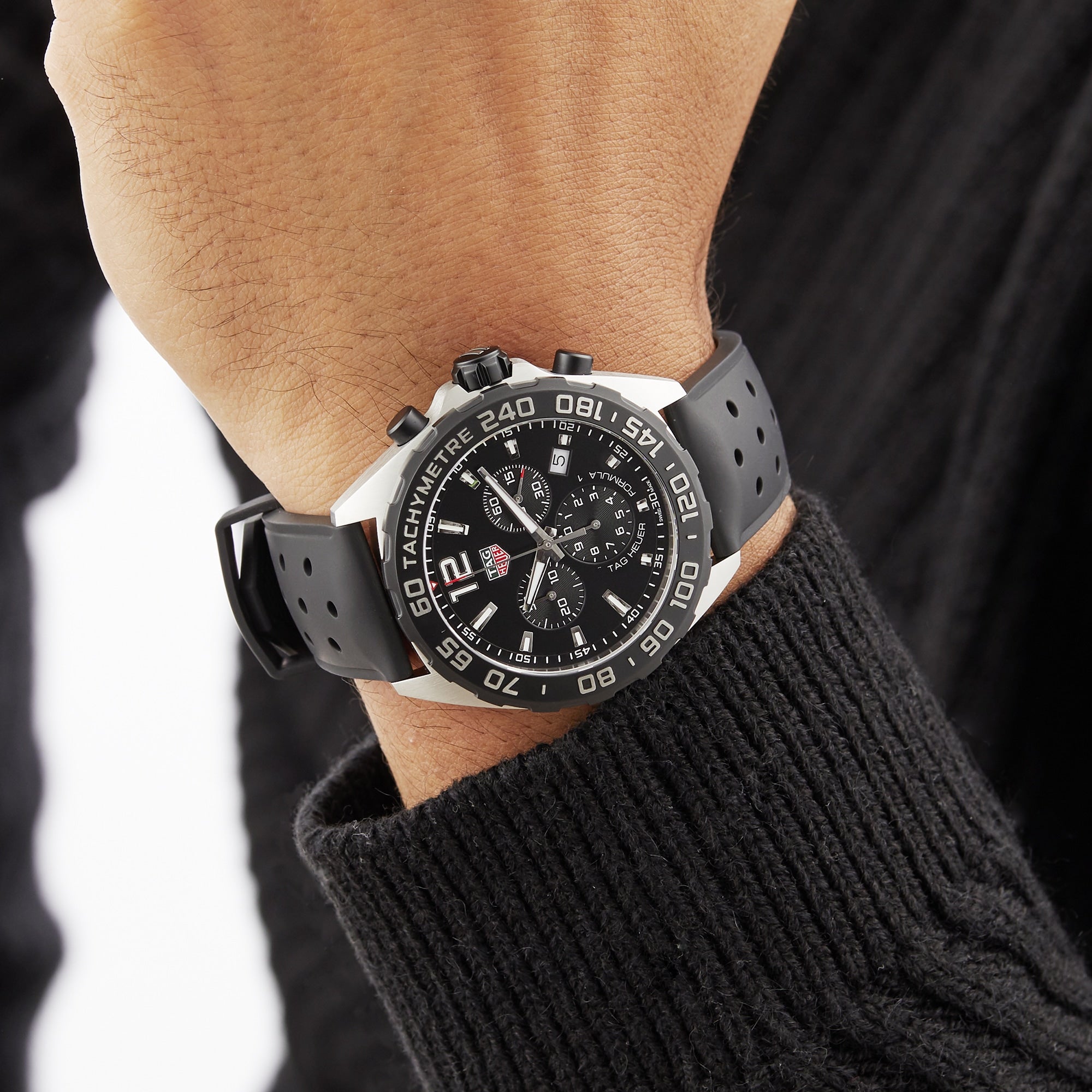 A person in a black sweater wears a TAG Heuer Formula 1 Chronograph with a black dial on their left wrist.