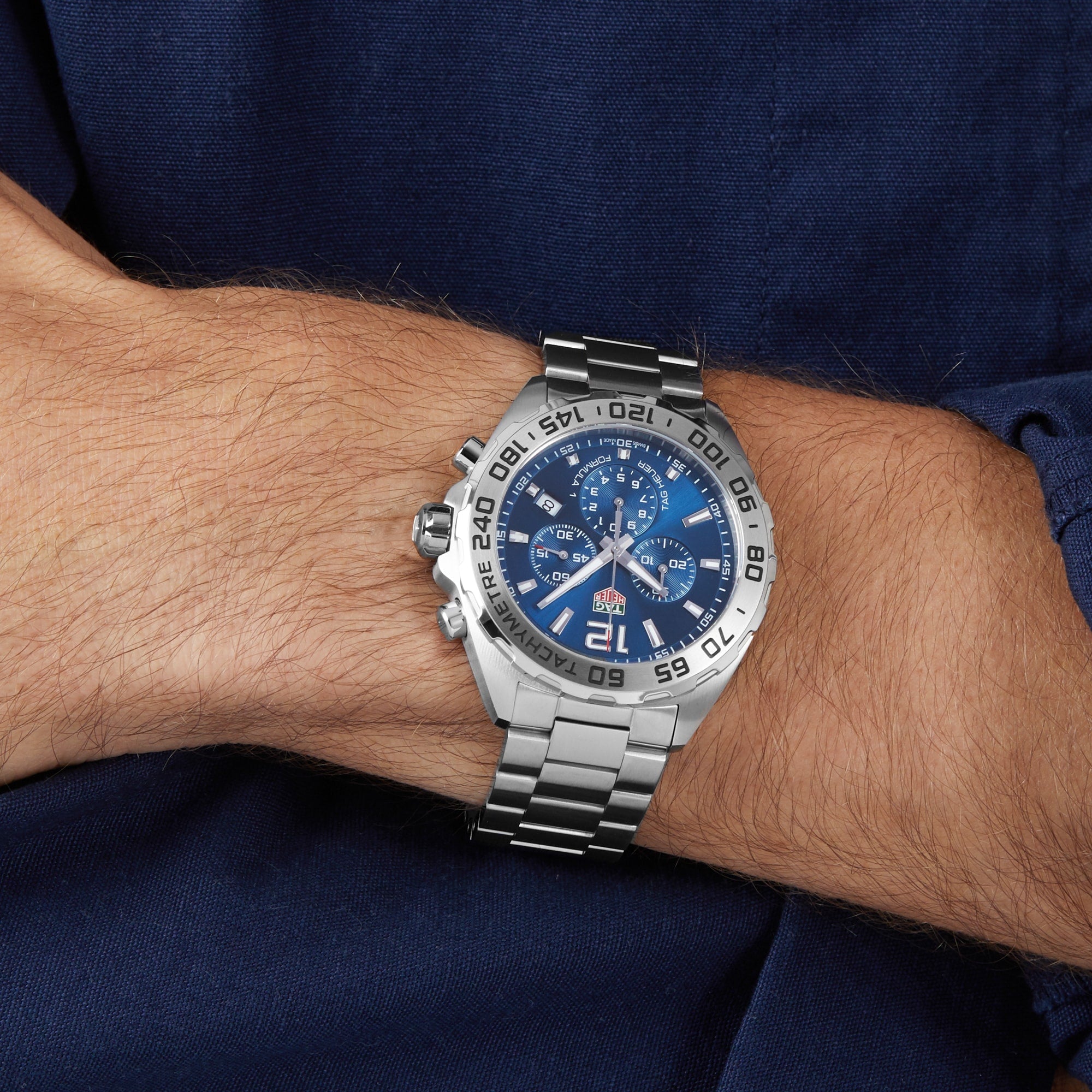 A TAG Heuer Formula 1 Chronograph watch is worn on a persons left wrist, paired with a dark blue shirt.