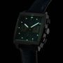 A TAG Heuer Monaco Chronograph watch with glowing green hour markers and hands in a dark setting.
