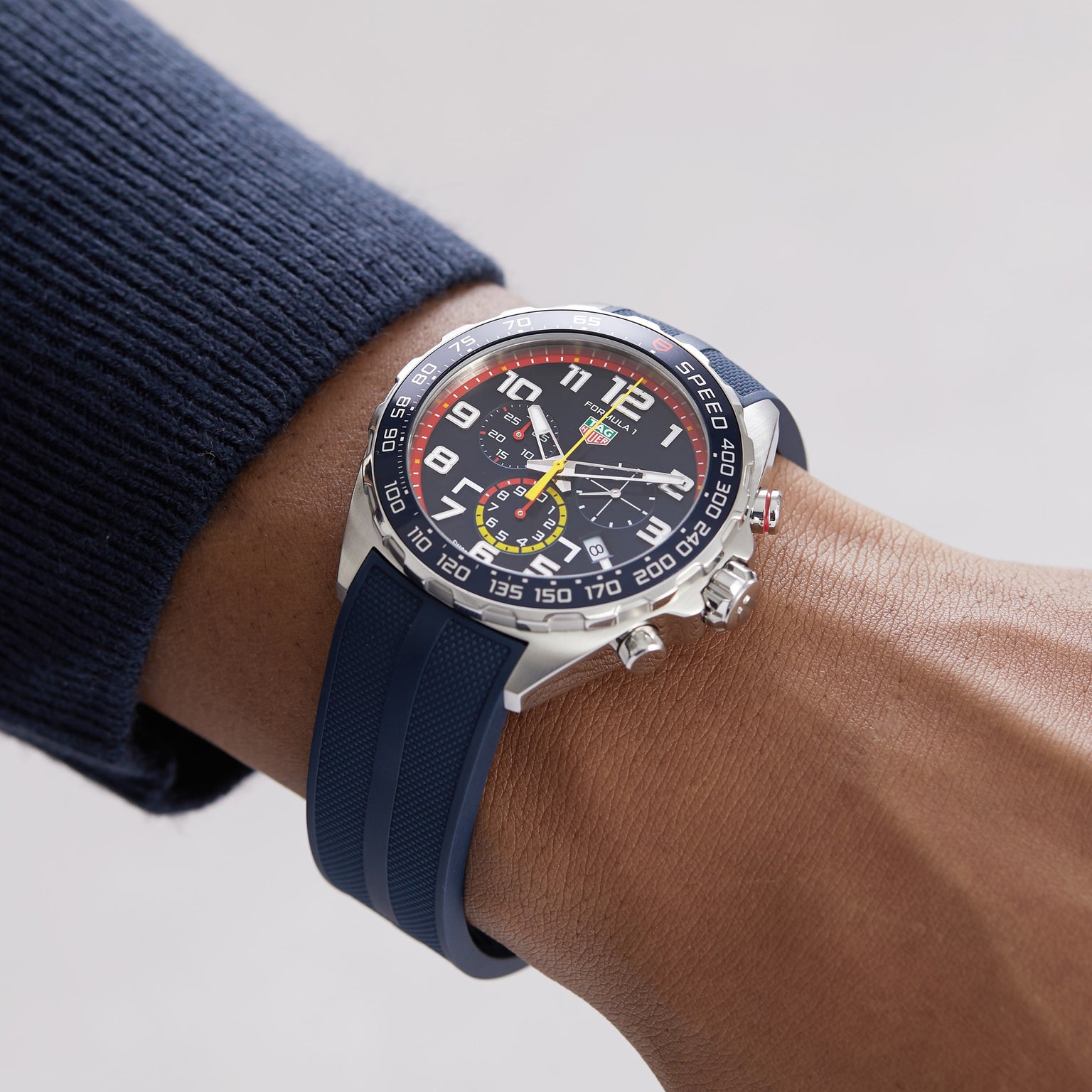 Someone wearing a TAG Heuer Special Edition Formula 1 Chronograph x Red Bull Racing watch, featuring a blue strap, black dial with colorful accents, and multiple subdials.
