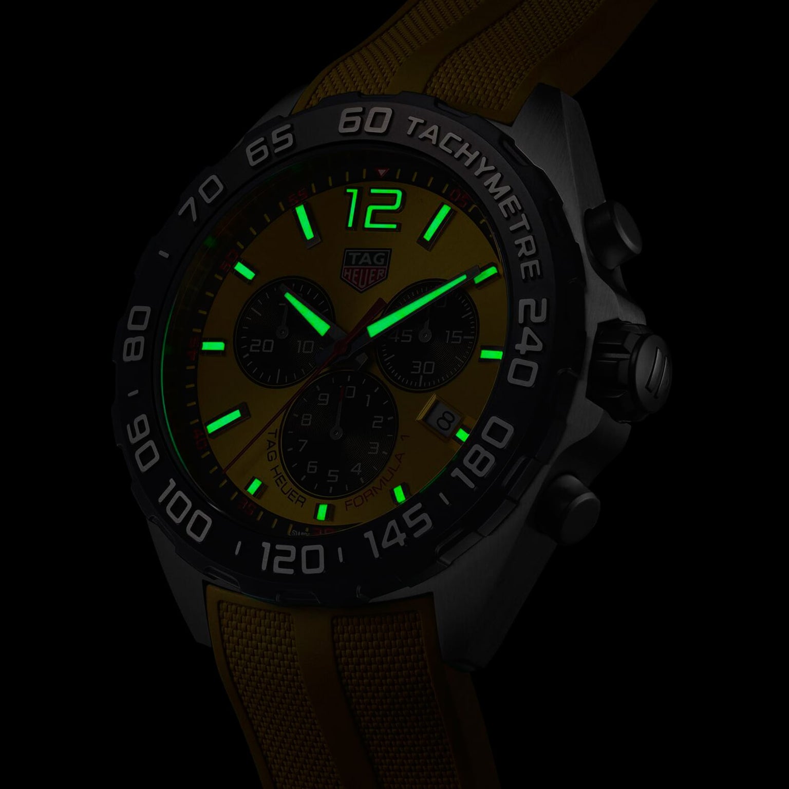 The TAG Heuer Formula 1 Chronograph wristwatch, shown in a dark setting, features a yellow face and strap, green luminescent markers and hands, quartz movement, and a tachymeter bezel.