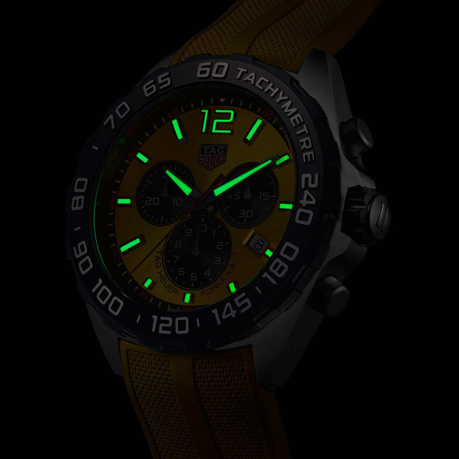 The TAG Heuer Formula 1 Chronograph wristwatch, shown in a dark setting, features a yellow face and strap, green luminescent markers and hands, quartz movement, and a tachymeter bezel.