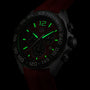 Close-up of a TAG Heuer Formula 1 Chronograph in low light, with green luminescent hands and numerals, stainless steel case, and partially visible red strap.