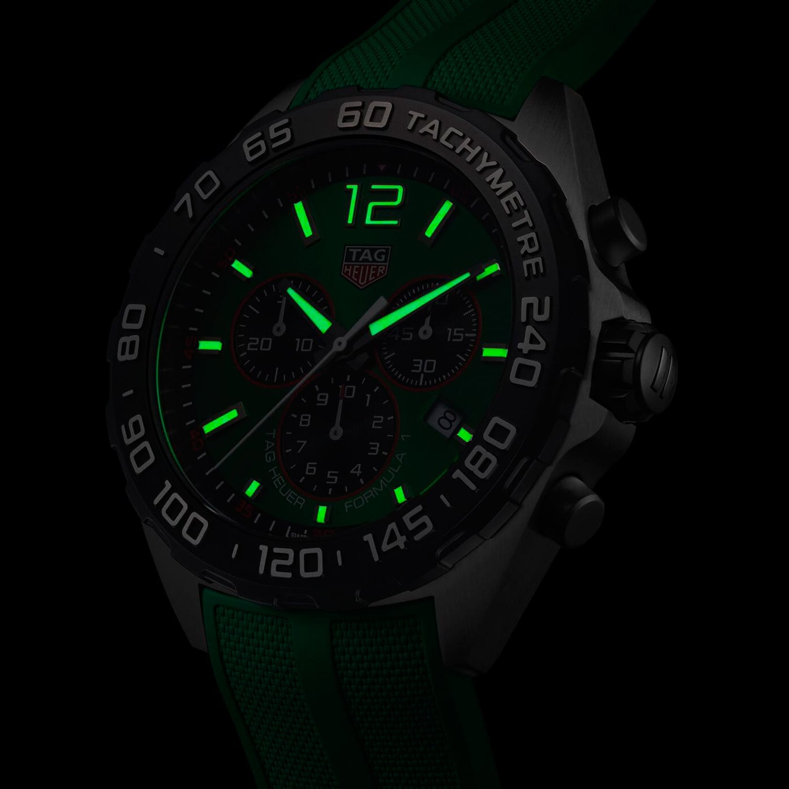 Close-up of a TAG Heuer Formula 1 Chronograph with a green strap, showcasing luminous green hands and numerals in low light. Powered by precise quartz movement.