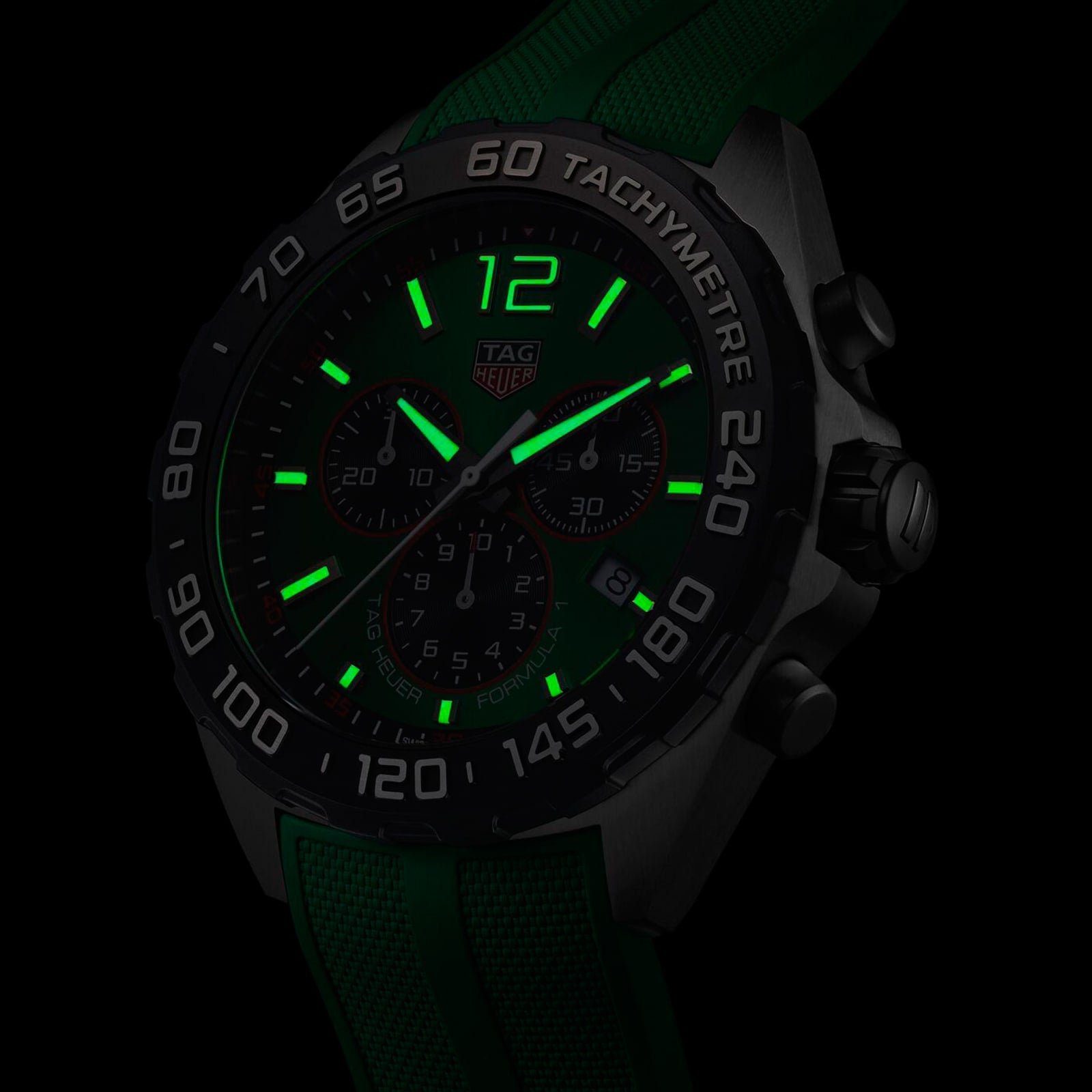 Close-up of a TAG Heuer Formula 1 Chronograph with a green strap, showcasing luminous green hands and numerals in low light. Powered by precise quartz movement.