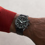 A TAG Heuer Autavia Flyback Chronometer with luminous hands and numerals, featuring a calibre 02 Flyback movement, is worn on the left wrist of a person in a red long-sleeve shirt.