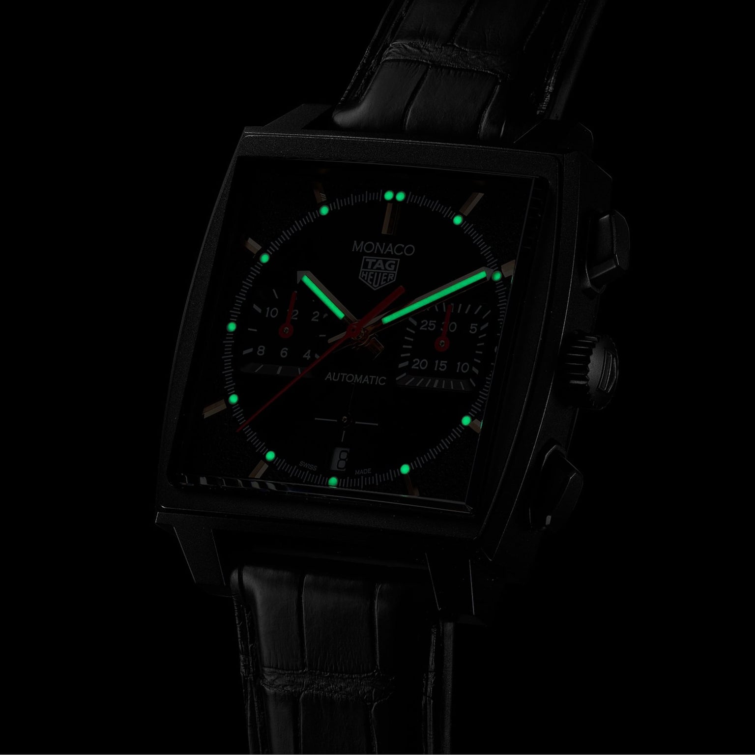 The TAG Heuer Monaco Chronograph features a black DLC titanium case, square face with luminescent markers, black leather strap, and runs on the advanced Heuer 02 movement—all set against a dark background.