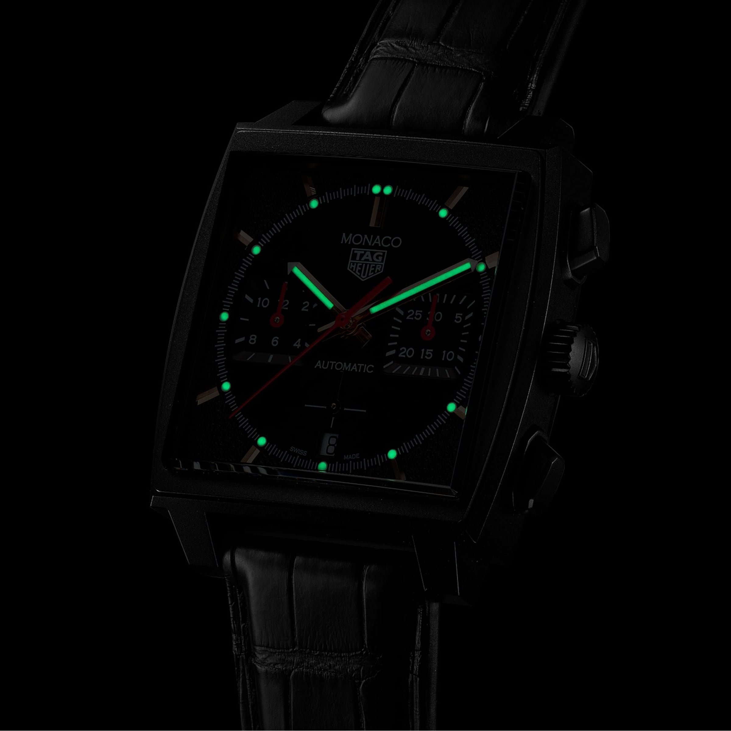 The TAG Heuer Monaco Chronograph features a black DLC titanium case, square face with luminescent markers, black leather strap, and runs on the advanced Heuer 02 movement—all set against a dark background.