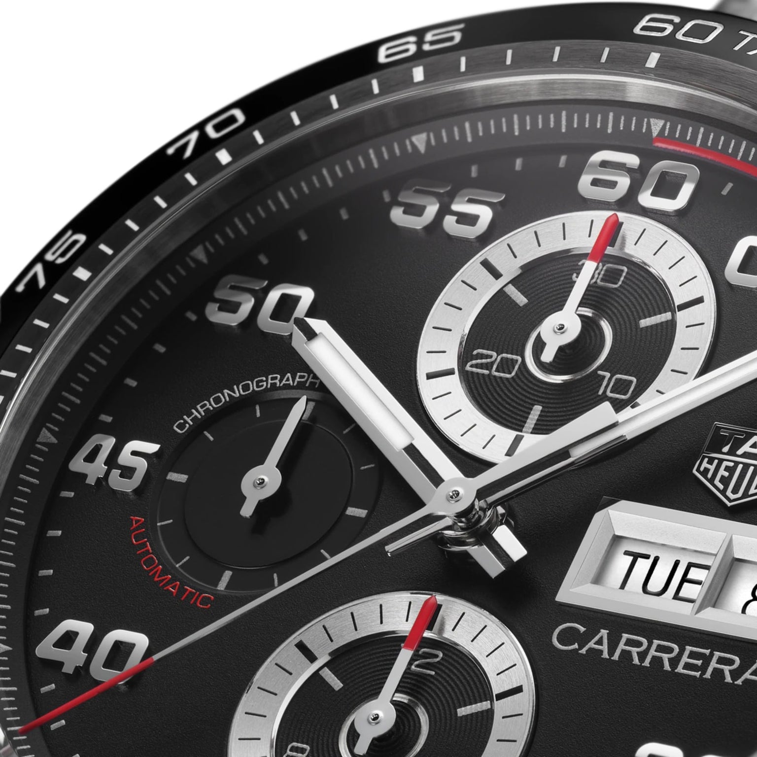 Close-up of the TAG Heuer Carrera Chronograph watch face, featuring a black ceramic bezel, three subdials, white hands, and a day-date window showing TUE 8.