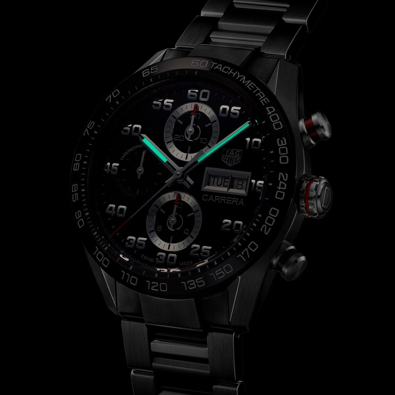 A TAG Heuer Carrera Chronograph watch with luminous hands, visible subdials, a ceramic bezel, and a metal bracelet is shown against a dark background.