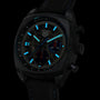 The TAG Heuer Monza Flyback Chronometer, COSC certified, flaunts a black skeleton dial with blue luminous markers and hands, plus a fabric strap—a tribute to motorsport—displayed against a black background.