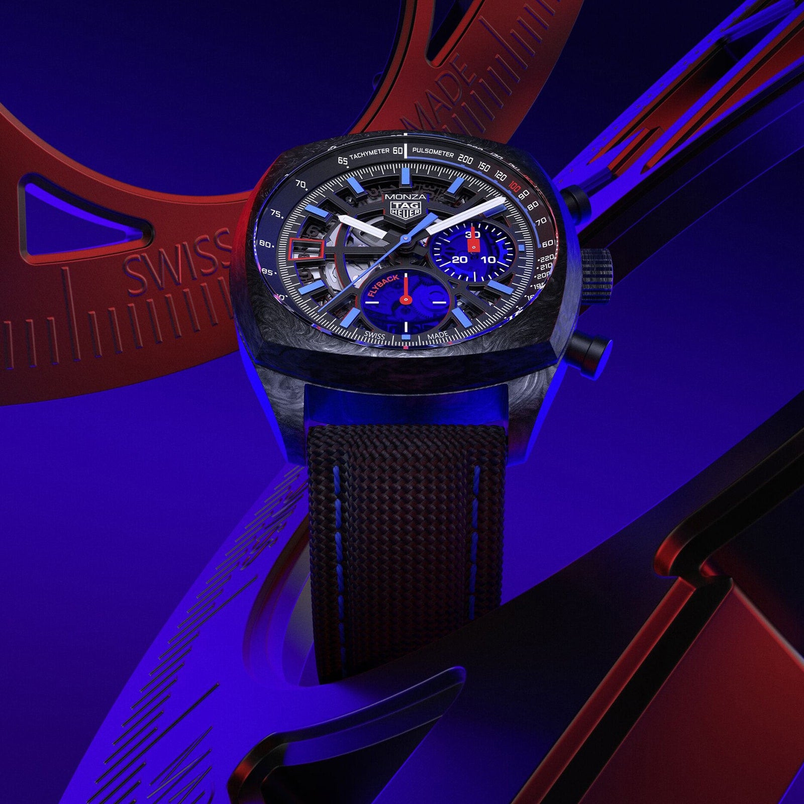 A TAG Heuer Monza Flyback Chronometer with a dark strap, set against a blue and red abstract background.