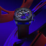A TAG Heuer Monza Flyback Chronometer with a dark strap, set against a blue and red abstract background.