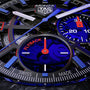 Close-up of the TAG Heuer Monza Flyback Chronometer watch face with chronograph subdials, Flyback text, COSC certified marking, Swiss Made at the bottom, and black, blue, and red accents inspired by competition motorsports.