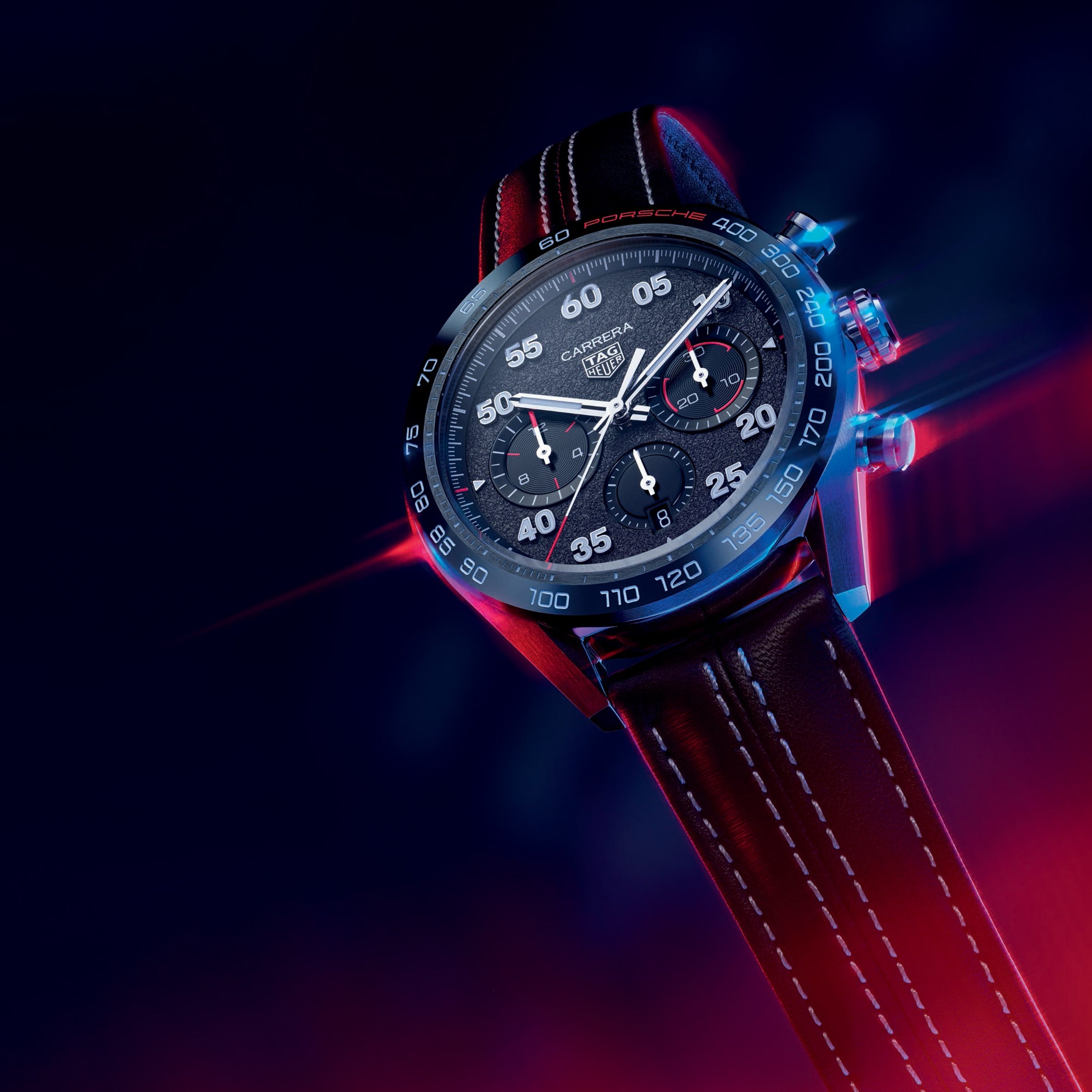 The TAG Heuer Special Edition Carrera Chronograph x Porsche features a black dial, red accents, and a brown leather strap, showcased against a neon-lit backdrop to capture the dynamic racing spirit of the TAG Heuer and Porsche collaboration.