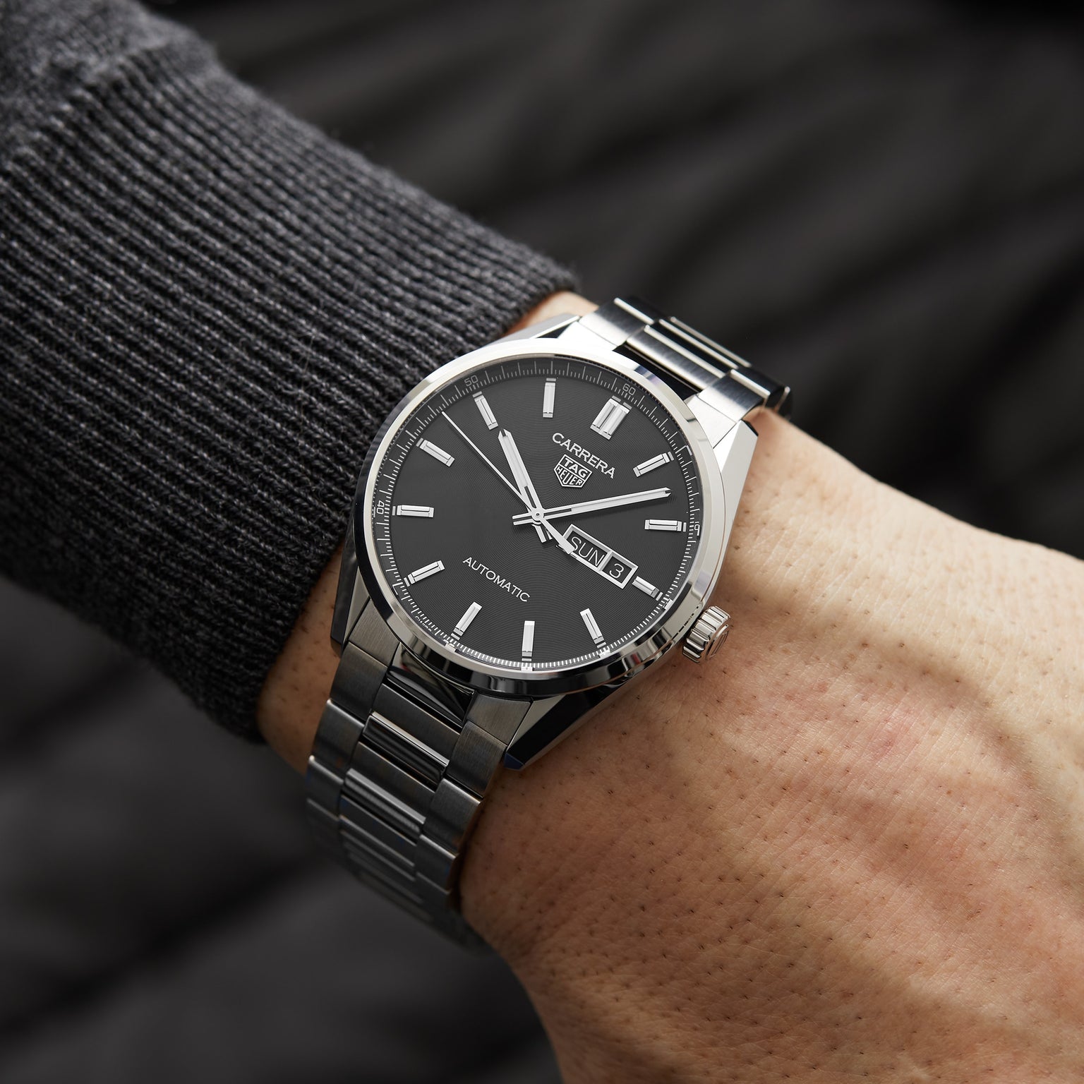 A person wearing a TAG Heuer Carrera Day-Date with a black azurage dial and calibre 5 automatic movement on their left wrist.