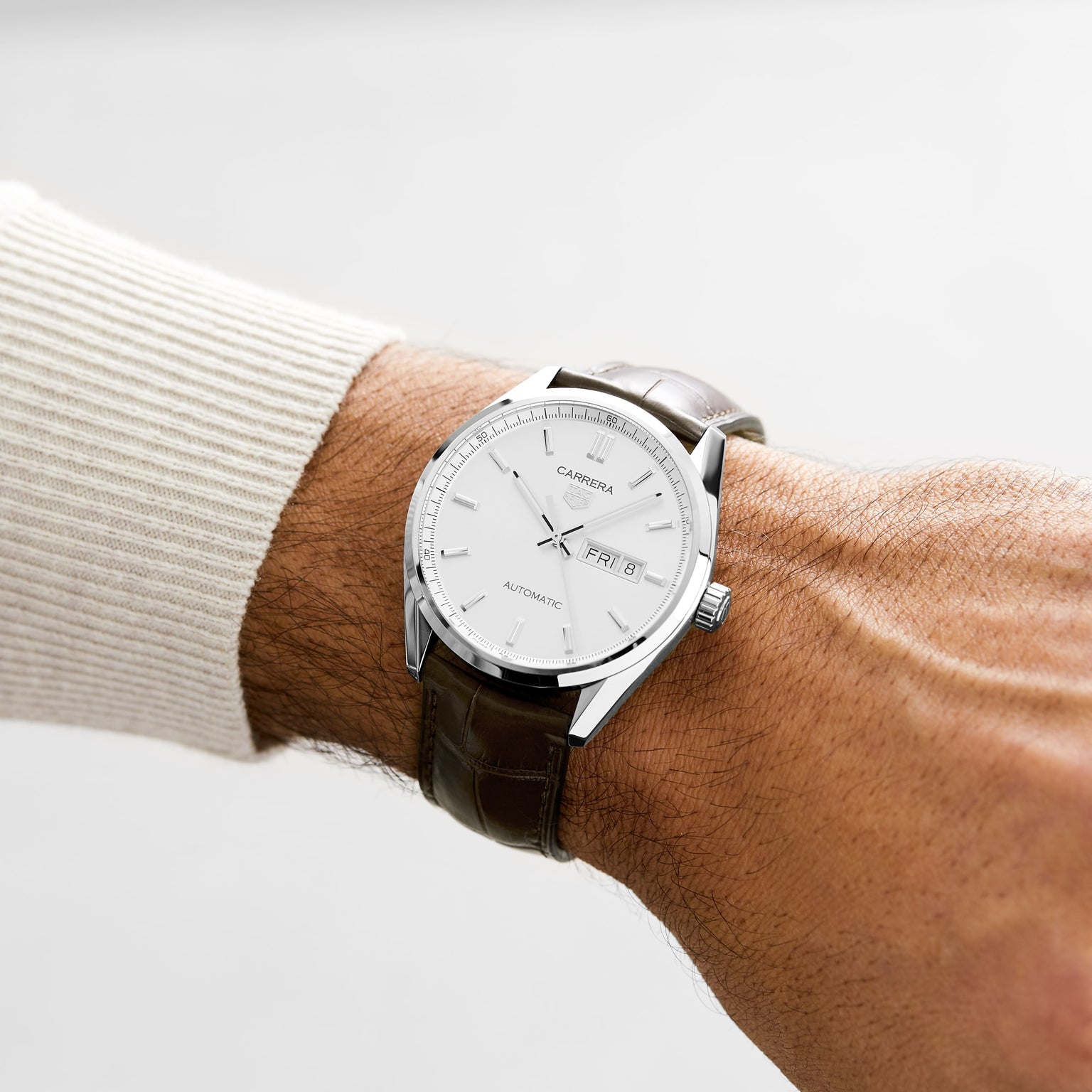 A person wearing a TAG Heuer Carrera Day-Date automatic watch with a white dial and brown alligator leather strap, displaying time, day, and date.