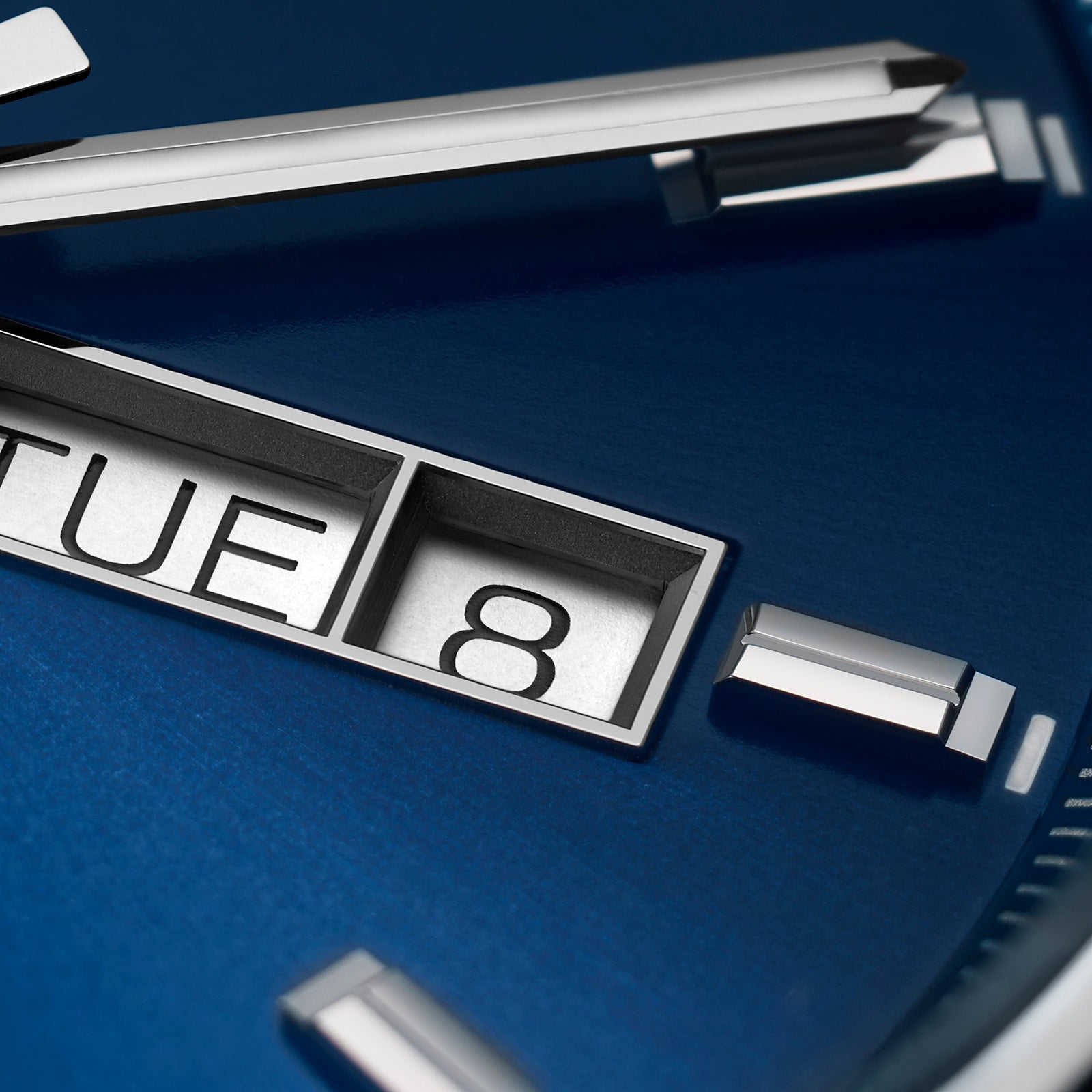 Close-up of the TAG Heuer Carrera Day-Dates blue sunray dial with silver hour markers and hands, day display at TUE, date at 8, powered by a Calibre 5 automatic movement.