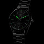 The TAG Heuer Carrera Date is a black watch with Calibre 5 automatic movement and a metal bracelet, featuring green luminescent hour markers and hands set against a dark background.