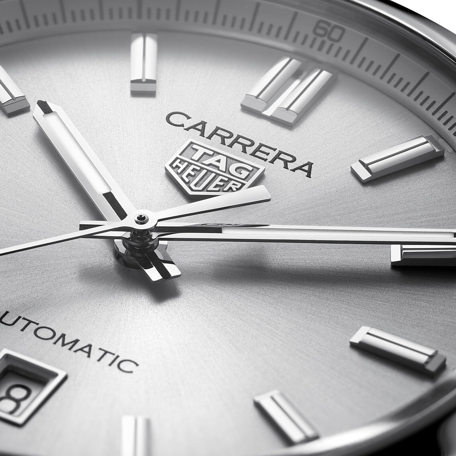 Close-up of the TAG Heuer Carrera Date watch face with silver markers, hands, and branding. The date window is visible, reflecting the legacy of the Carrera Panamericana race.