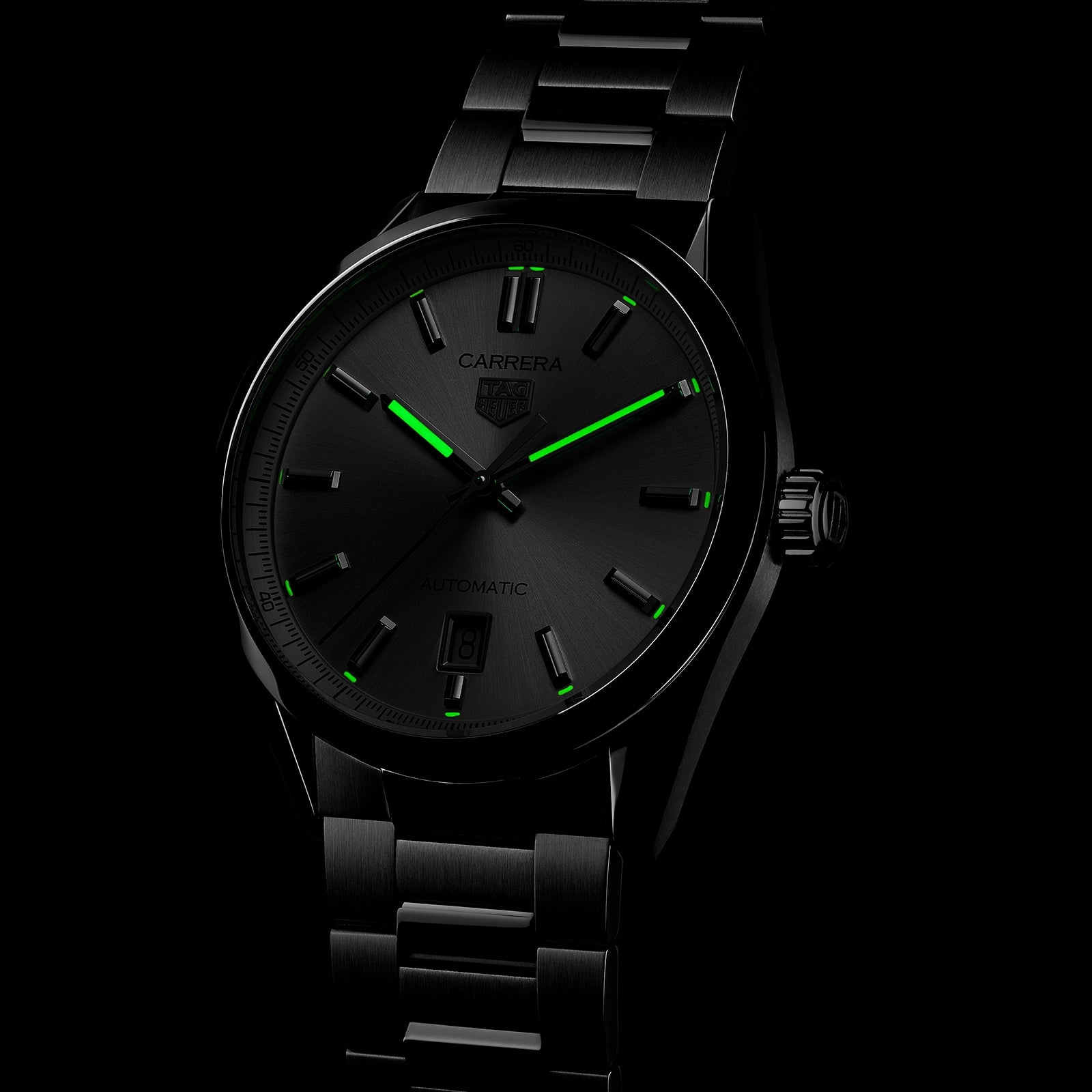 The TAG Heuer Carrera Date is a black metal wristwatch with green luminescent markers and hands, a date display at 6 o’clock, calibre 5 automatic movement, and CARRERA and TAG Heuer logos on the black dial—celebrating Carrera Panamericana.