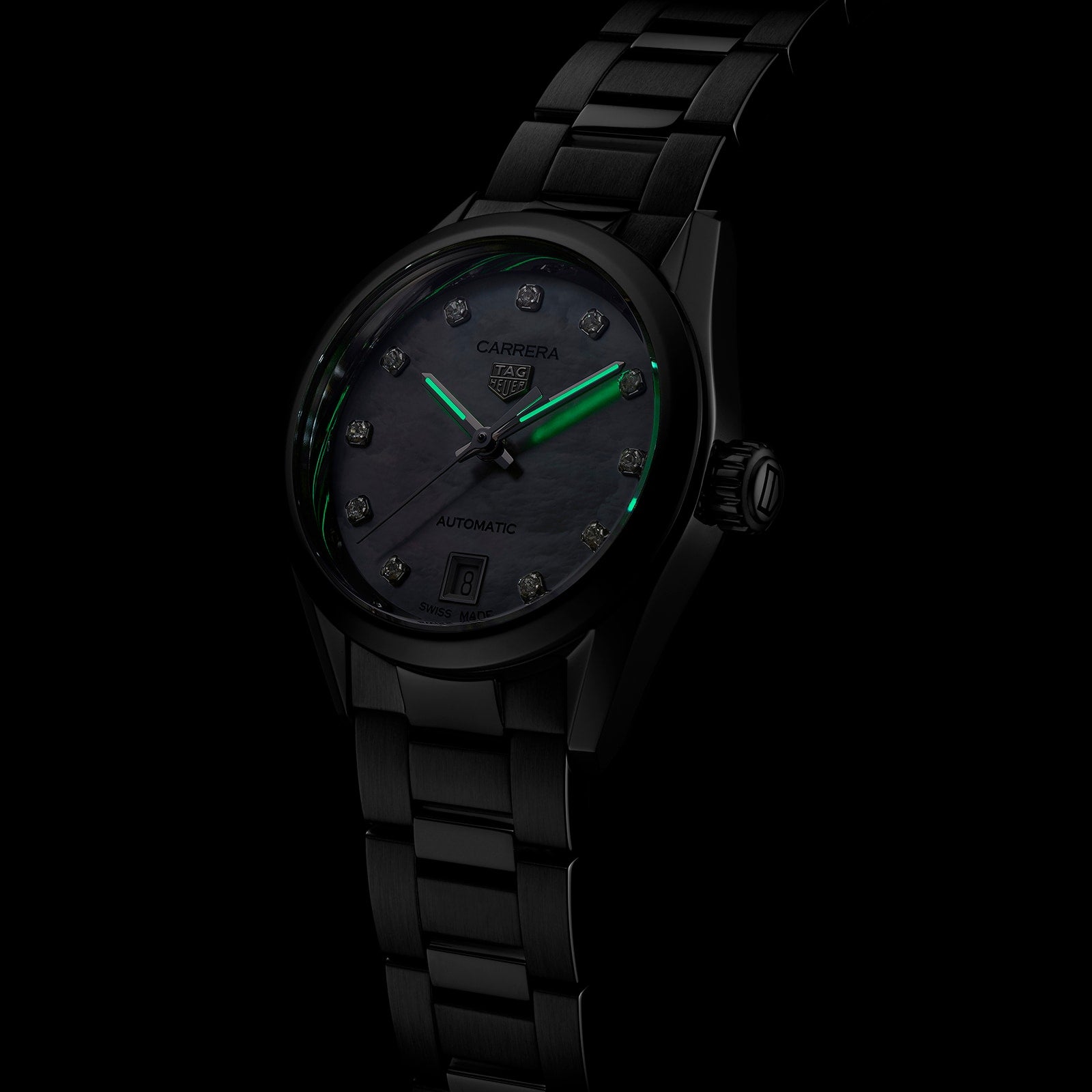 The TAG Heuer Carrera Date is a black metal wristwatch with a dark face, diamond hour markers, date display, and green luminescent hour and minute hands.