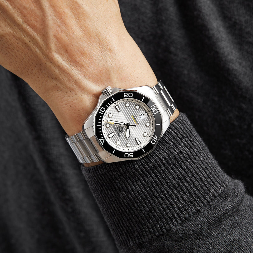 A person in a dark long-sleeve shirt wearing the TAG Heuer Aquaracer Professional 300 Date, featuring a stainless steel case, black and silver bezel, and a silver textured dial.