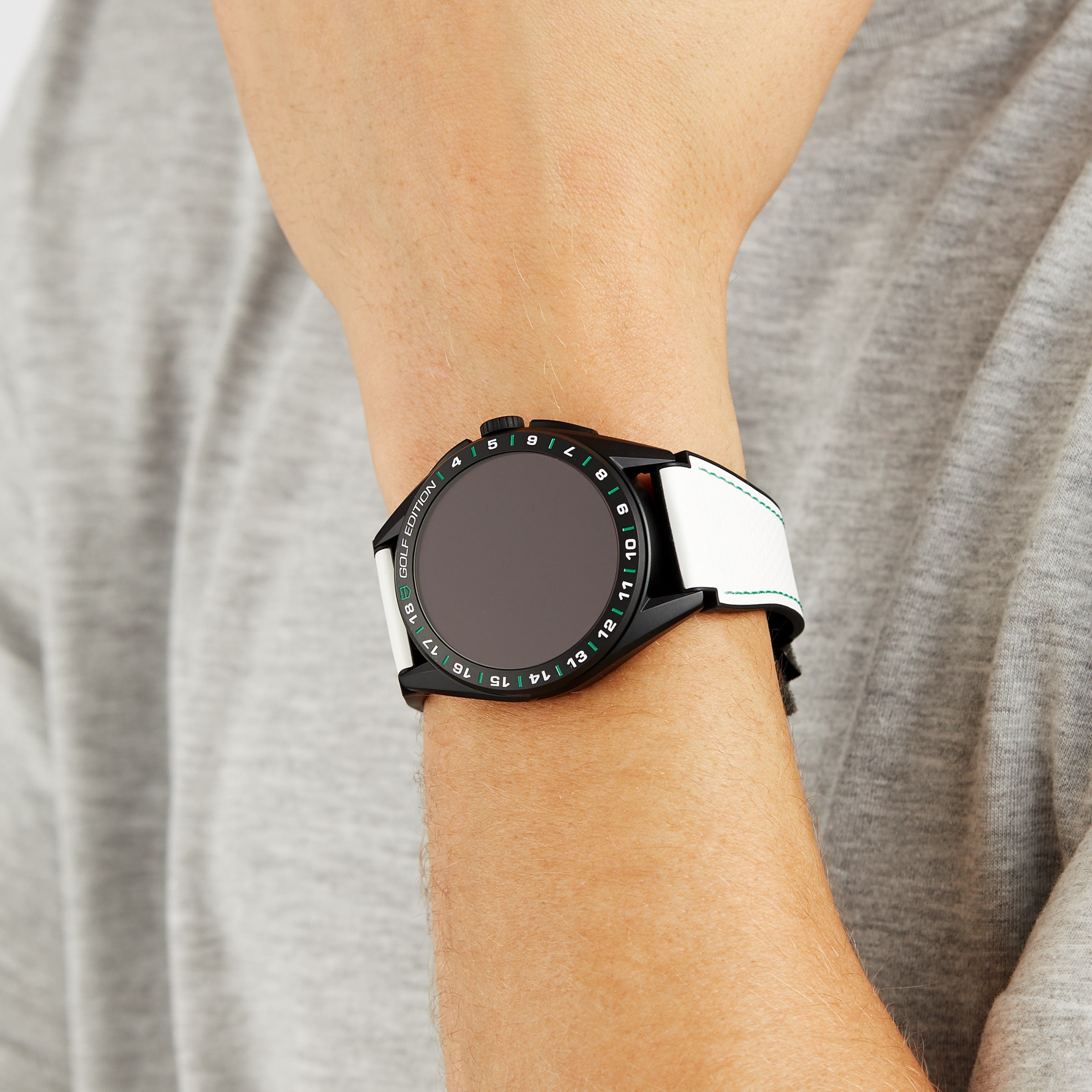 A person wearing a TAG Heuer Connected Calibre E4 Golf Edition with a round face and white strap on their left wrist.