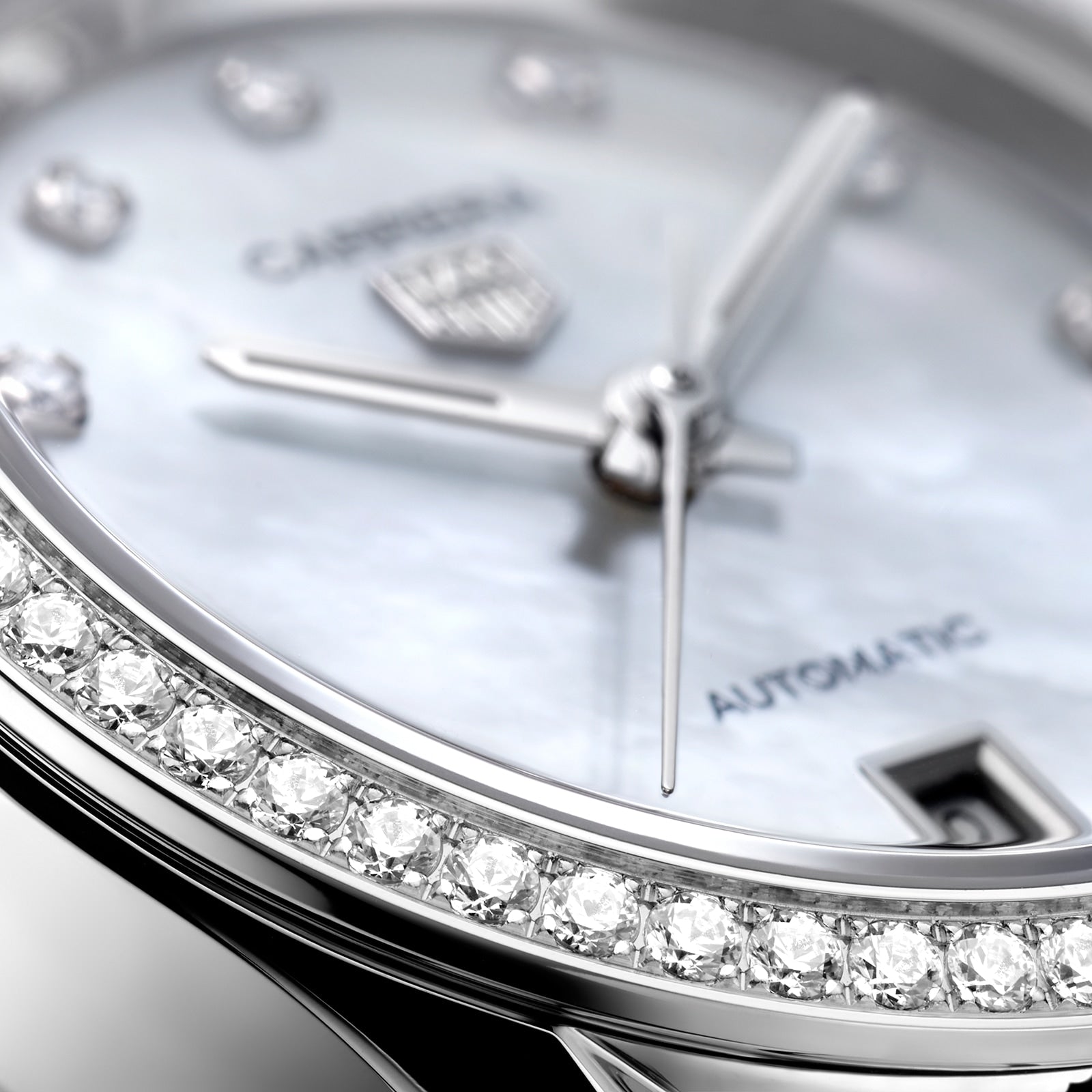 Close-up of a TAG Heuer Carrera Date wristwatch featuring a diamond bezel, silver hands, and a date window on a white dial marked with Carrera and Automatic.
