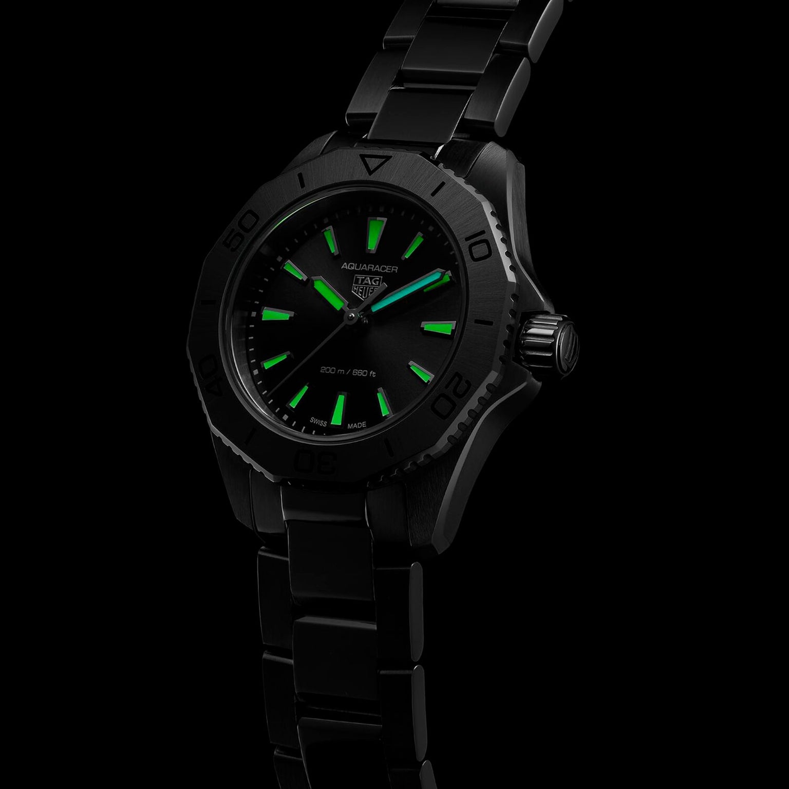 The TAG Heuer Aquaracer Professional 200 is a black sports watch with a stainless steel case, metal band, and luminous green hour markers and hands, shown against a black background.
