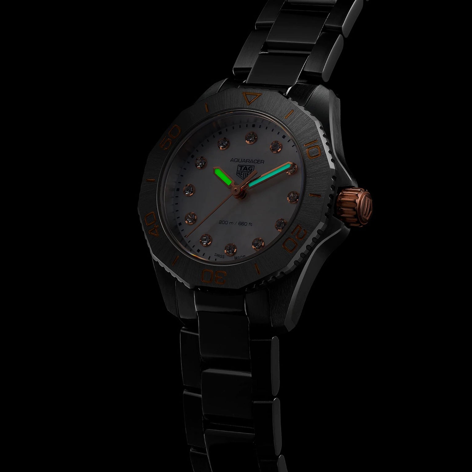 A TAG Heuer Aquaracer Professional 200 wristwatch with a stainless steel case, black metal band, dark dial with orange accents, and luminous hands is photographed against a black background.