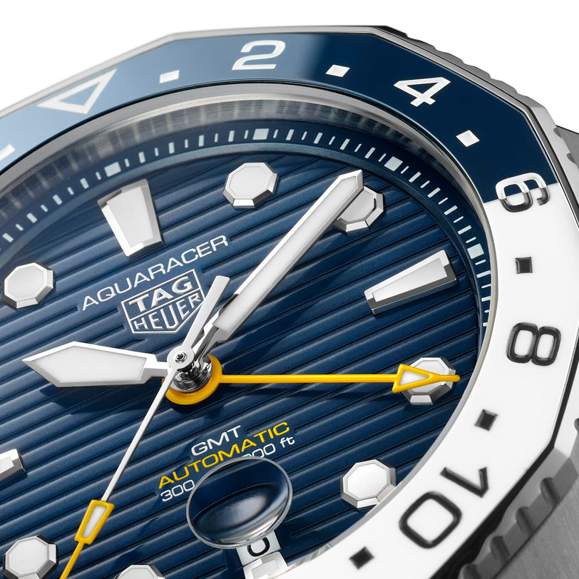 Close-up of the TAG Heuer Aquaracer Professional 300 GMT watch face featuring a blue textured dial, white markers, yellow GMT hand, and the text GMT AUTOMATIC 300m/1000ft.
