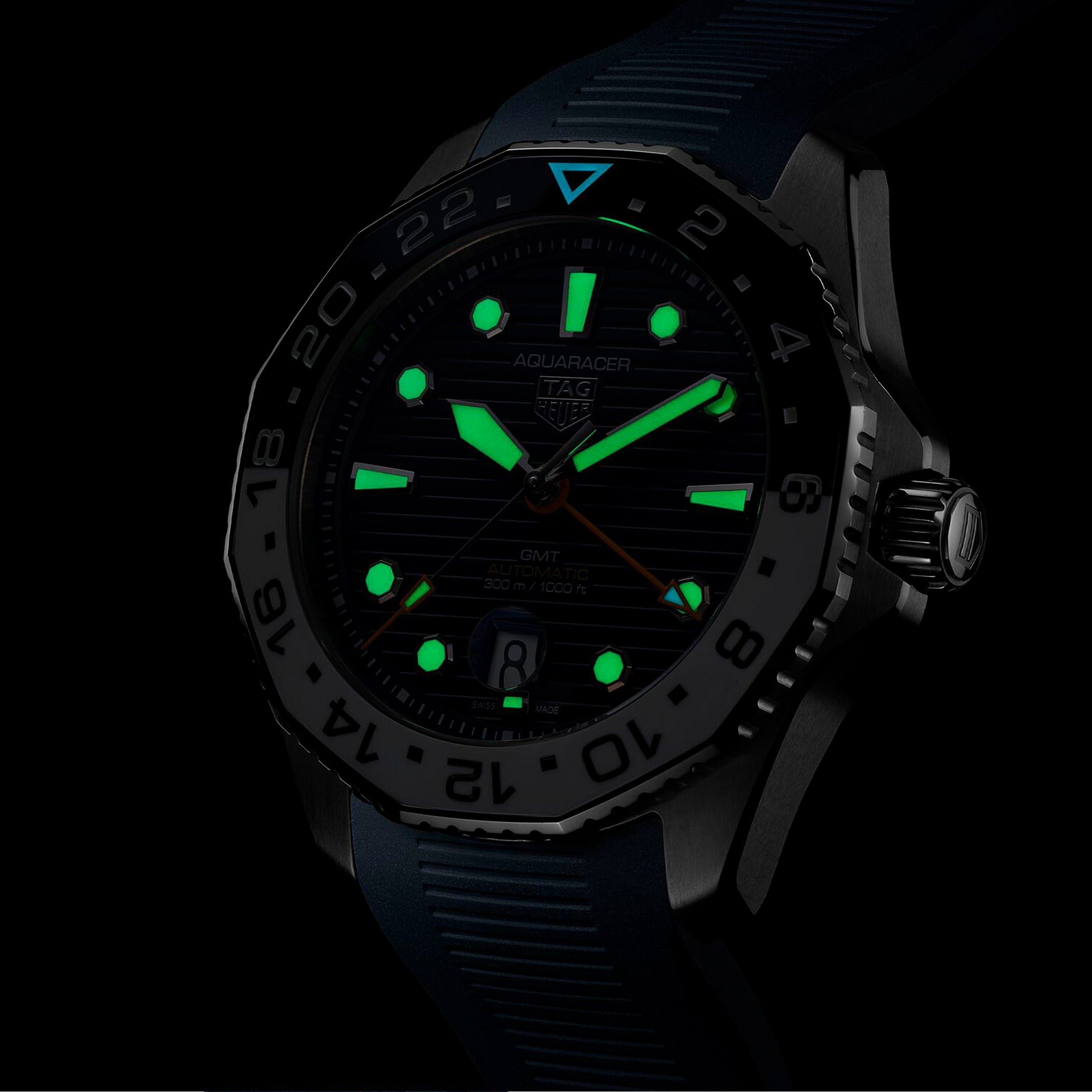 The TAG Heuer Aquaracer Professional 300 GMT sports watch features a black dial with luminous green hands and hour markers, glowing brightly in low-light conditions.