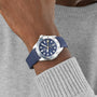 A close-up of a person wearing the TAG Heuer Aquaracer Professional 300 GMT with a blue strap and patterned blue dial, paired with a light grey knit sweater.