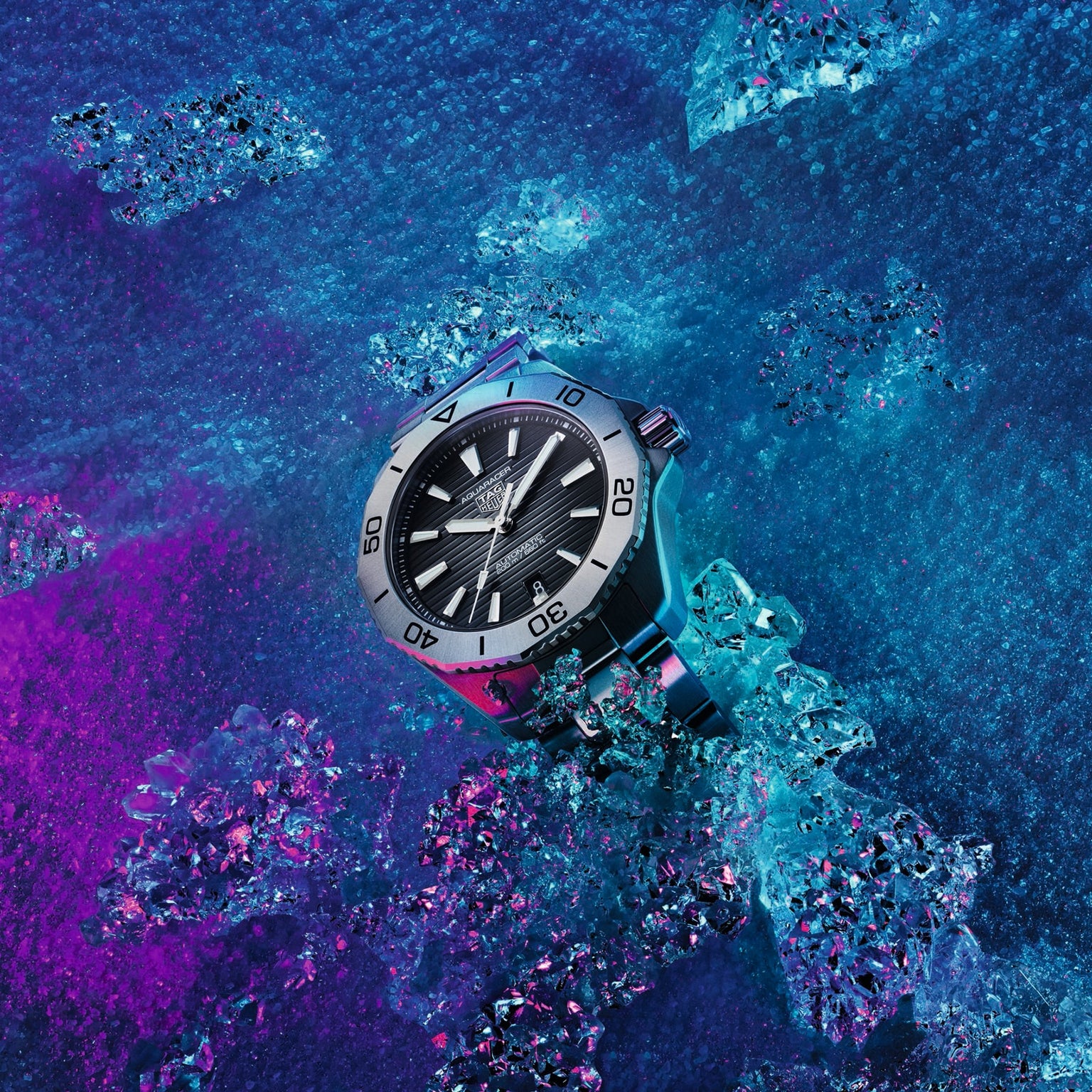 A TAG Heuer Aquaracer Professional 200 Date wristwatch with a silver case, black face, and bold markers sits on blue and purple ice among scattered crystals—driven by automatic Calibre 5 for professional precision.