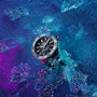 A TAG Heuer Aquaracer Professional 200 Date wristwatch with a silver case, black face, and bold markers sits on blue and purple ice among scattered crystals—driven by automatic Calibre 5 for professional precision.
