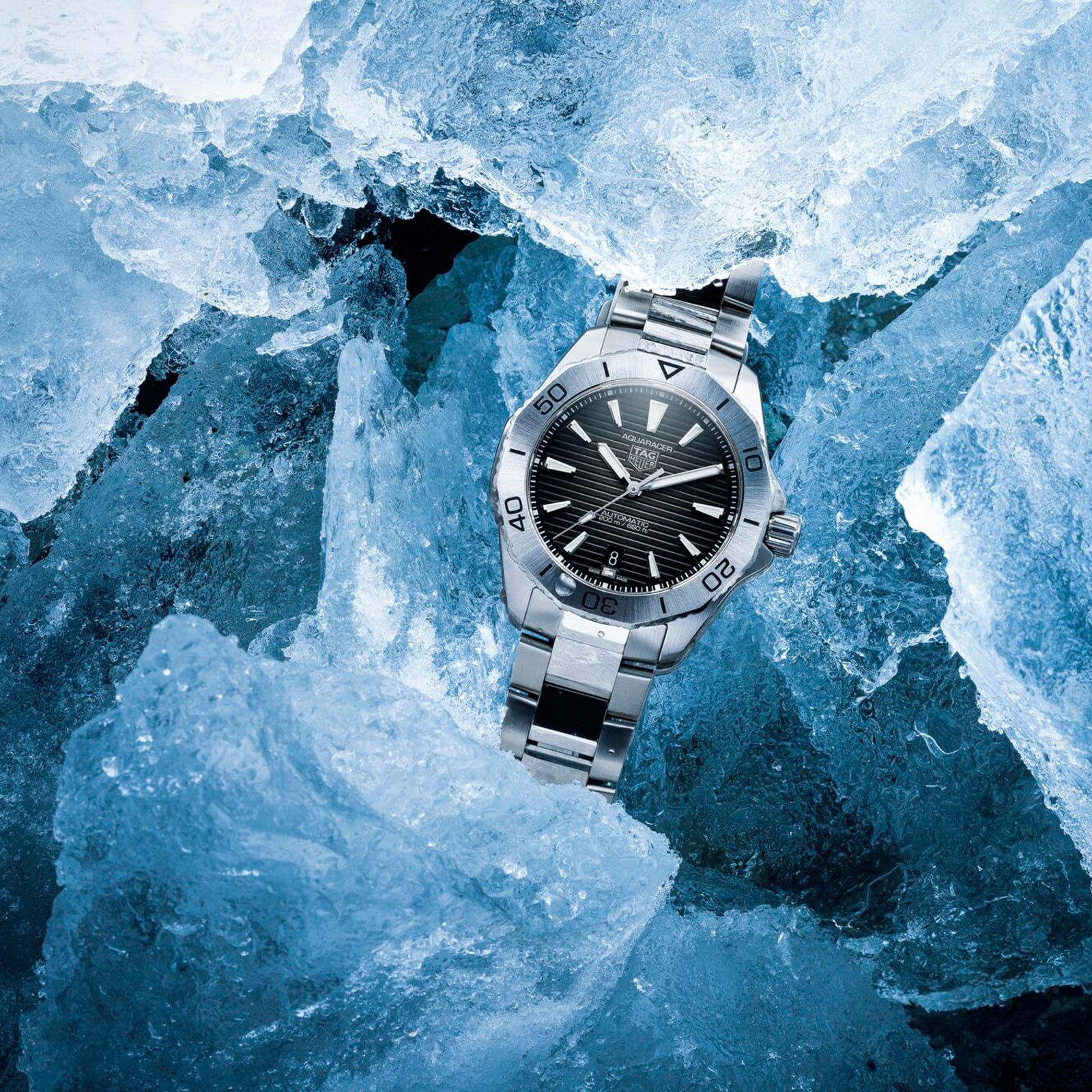 A TAG Heuer Aquaracer Professional 200 Date wristwatch with a black dial rests among large chunks of ice.