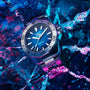 The TAG Heuer Aquaracer Professional 200 Date, a silver and blue diving watch with a stainless steel case, sits on cracked ice under vibrant blue and pink lighting.