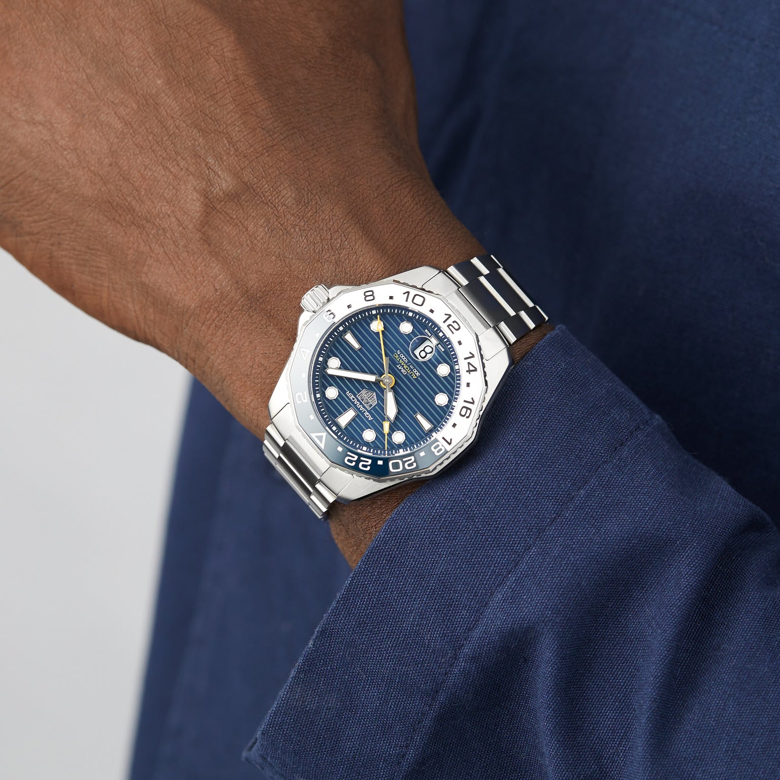 A person wearing a TAG Heuer Aquaracer Professional 300 GMT silver wristwatch with a blue dial and a blue long-sleeve shirt.