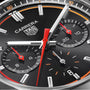 Close-up of the TAG Heuer Carrera Chronograph watch face with a black dial, three subdials, a date window, and red accents on the hands. Features precision Calibre HEUER 02 movement.