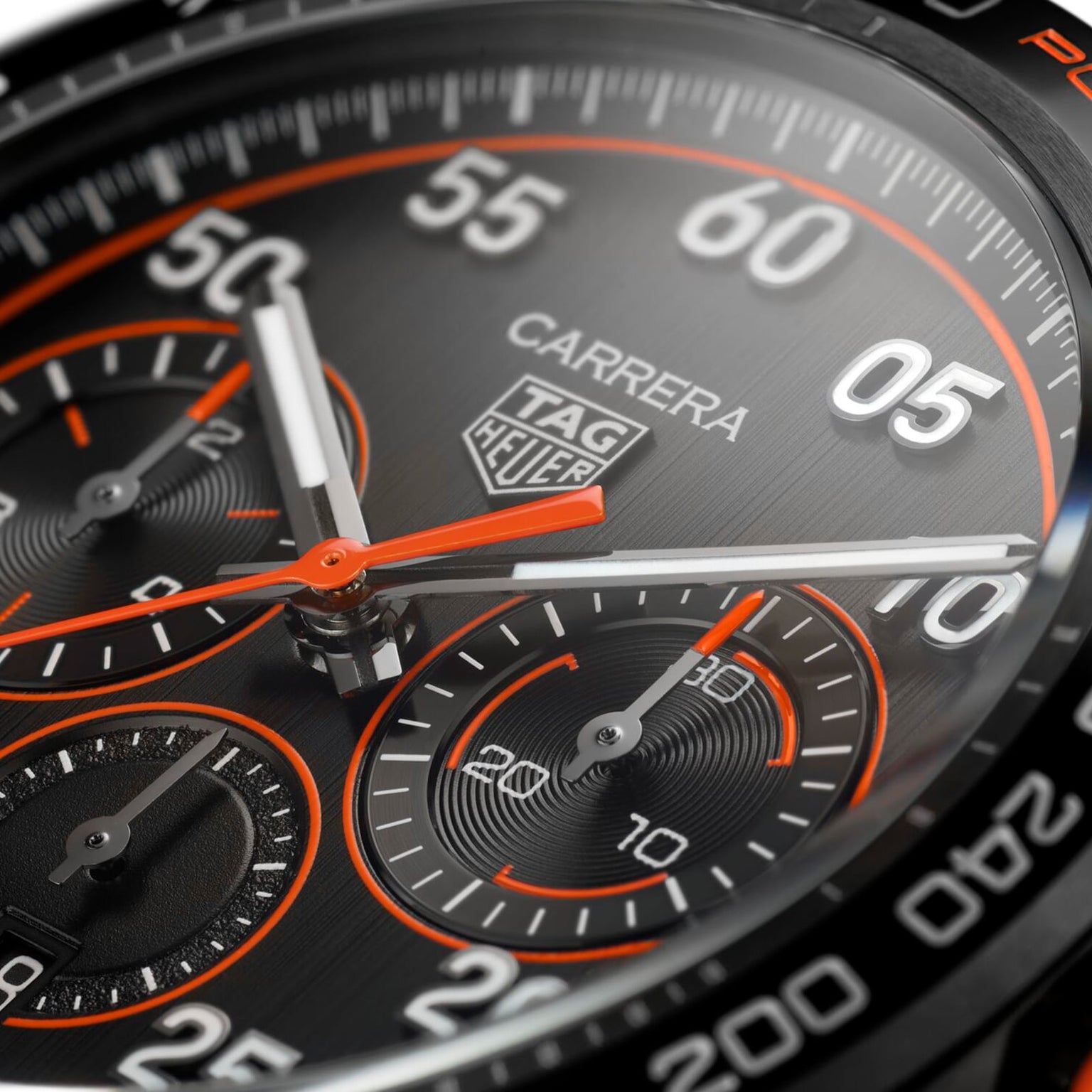 Close-up of the TAG Heuer Special Edition Carrera Chronograph x Porsche Orange Racing watch face, showcasing chronograph dials, orange accents, and bold white numerals on a brushed metal background.