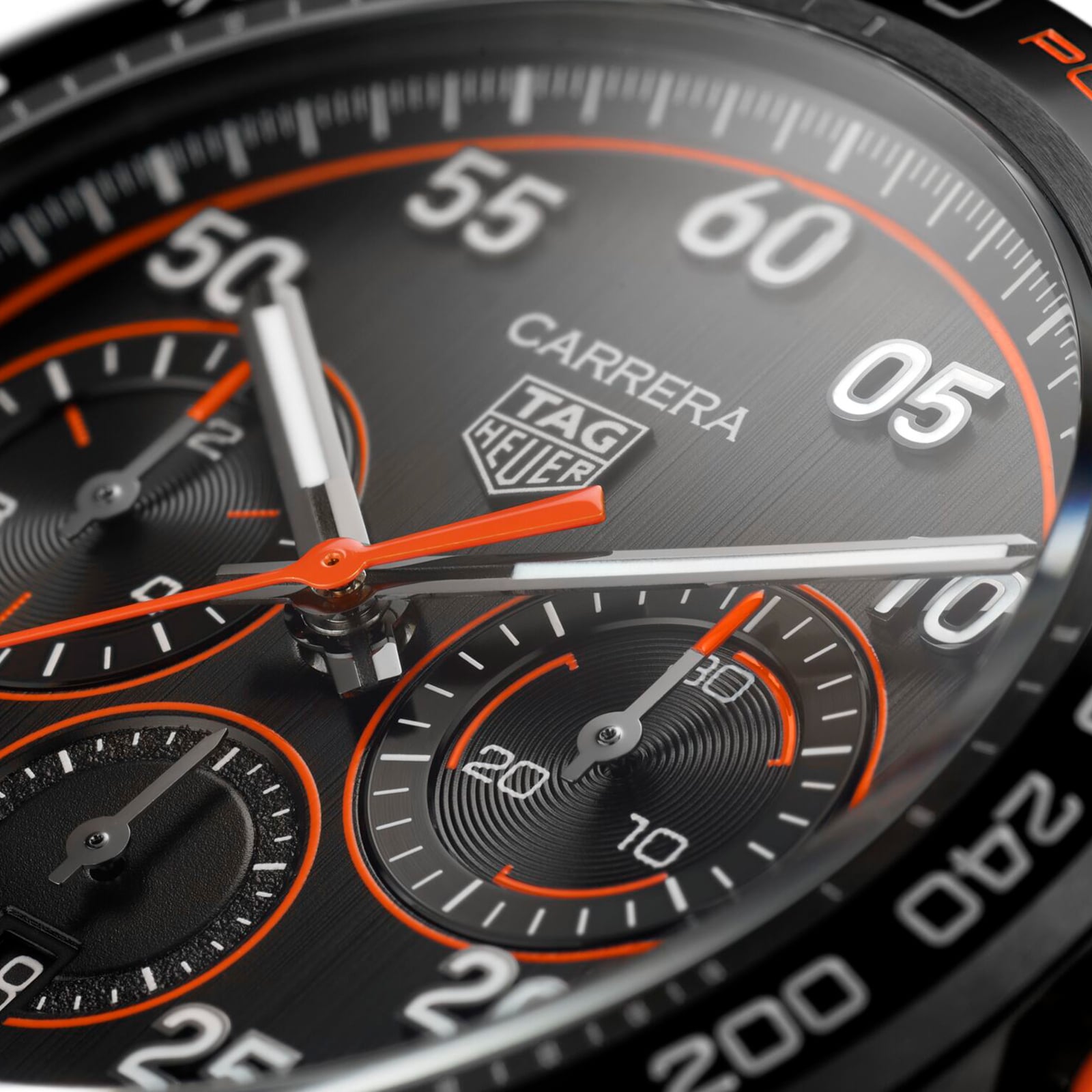 Close-up of the TAG Heuer Special Edition Carrera Chronograph x Porsche Orange Racing watch face, showcasing chronograph dials, orange accents, and bold white numerals on a brushed metal background.