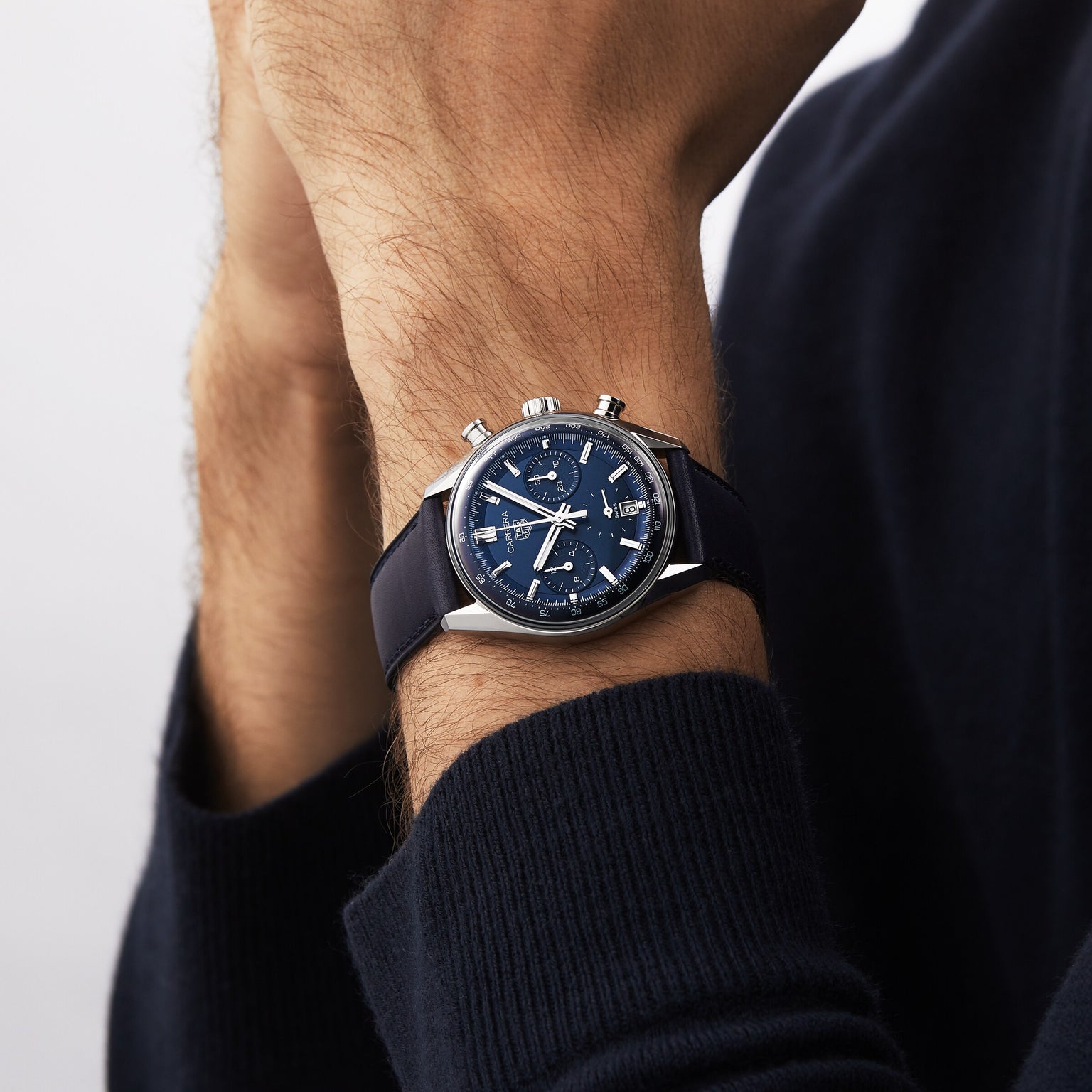 A person wearing a TAG Heuer Carrera Chronograph with a navy blue dial and leather strap rests their hand against their chin.