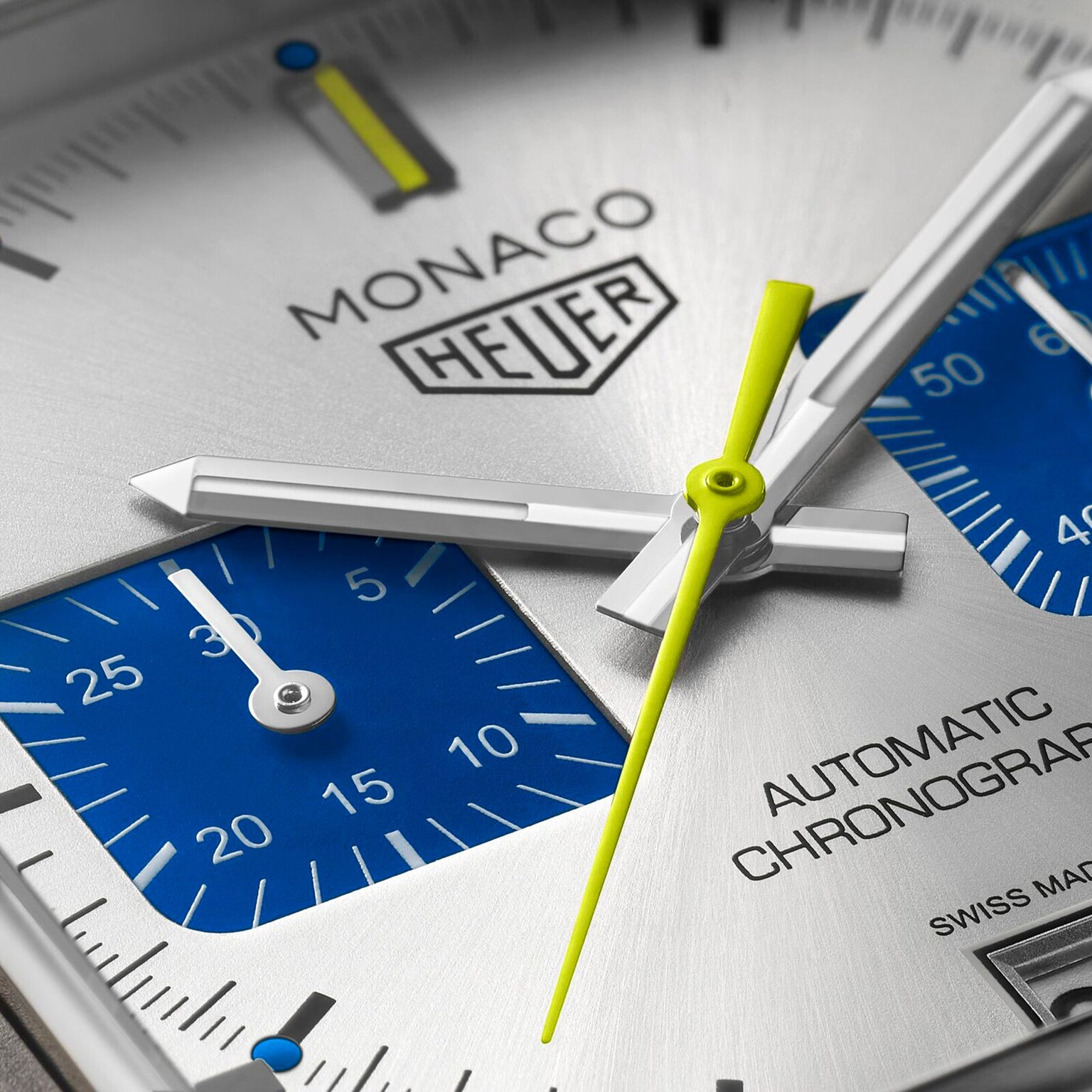 Close-up of a TAG Heuer Limited Edition Monaco Chronograph French Racing Blue watch face, showing silver hour and minute hands, a yellow second hand, blue subdials, and the text Monaco Heuer Calibre 11 Automatic Chronograph.